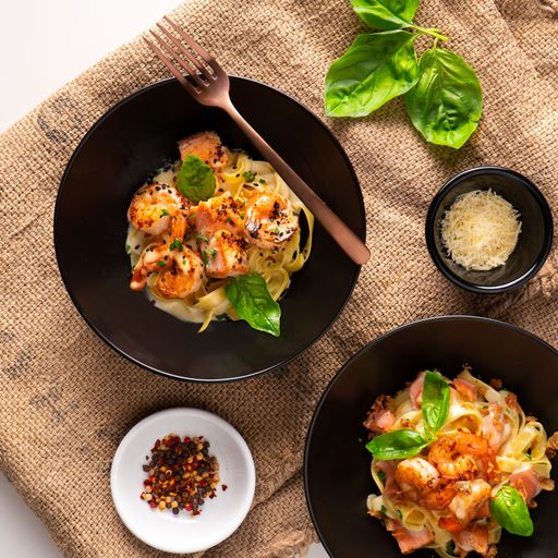 A top view of the spaghetti with seafood seasoned with different ingredients in the black bowls on a brown towel