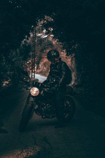 A cool biker with a leather jacket sitting on his motorcycle in a dark tunnel of trees in the woods