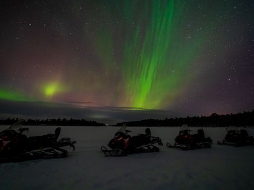 A beautiful landscape of polar lights in the night sky over the snowmobiles