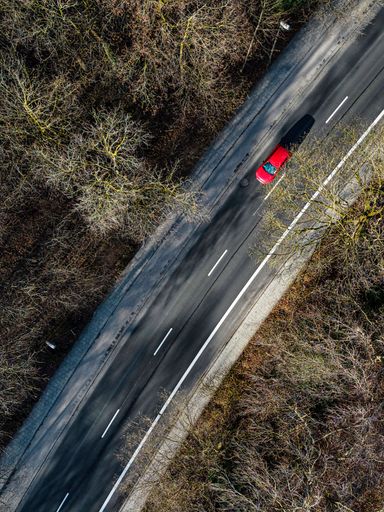An aerial shot of a car driving along a rural road, surrounded by trees and greenery