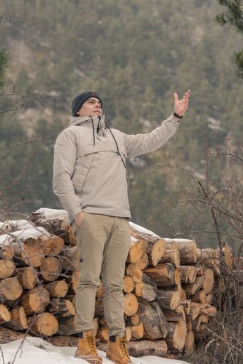 A young man with beige outfit in the field on firewood in winter with snow.