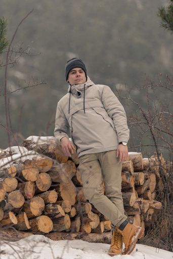 A young man with beige outfit in the field on firewood in winter with snow