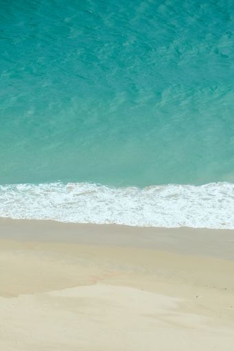 A vertical shot of a sandy beach coastline, with soft, rolling waves of the ocean lapping onto the shore