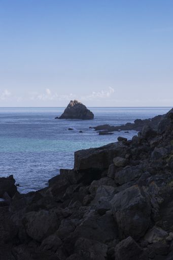 A vertical shot of a beautiful rocks alongside and inside the ocean under the bright sky
