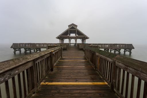 A wooden pier extending out across a tranquil body of water surrounded by a thick fog