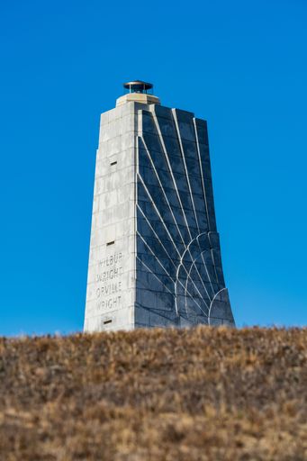 A vertical shot of the Wright Brothers National Memorial set against bright blue sky