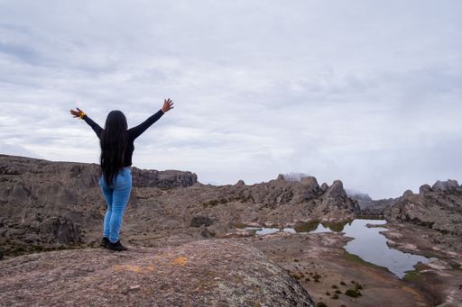A woman stands on a rock with arms open wide in appreciation of nature's beauty. Peru.