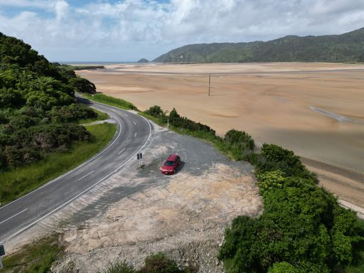 A landscape view of the red car on the narrow road with a sandy area and hills in the back