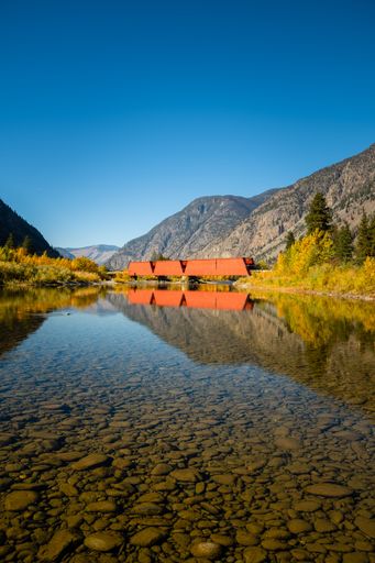 A closeup shot of the clean water and the stones under the Similkameen river with a red bridge.