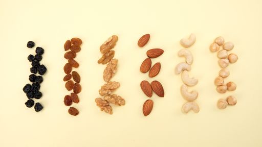 A high angle shot of rows of different nuts and seeds on a yellow surface