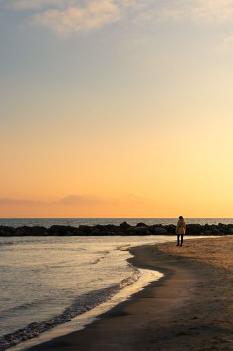 A person walking along a beach in the early morning light, with an expansive ocean in the background