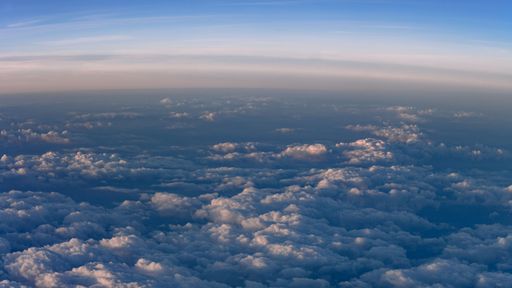 View from the plane. The sun is setting and shines a warm light on the clouds.