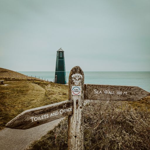 A scenic view of a lighthouse at Samphire Hoe with a direction sign and a coastline in the distance