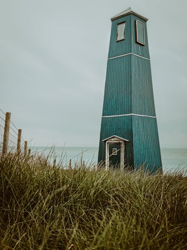 A scenic view of a lighthouse at Samphire Hoe situated near a grassy area with a coastline in the distance