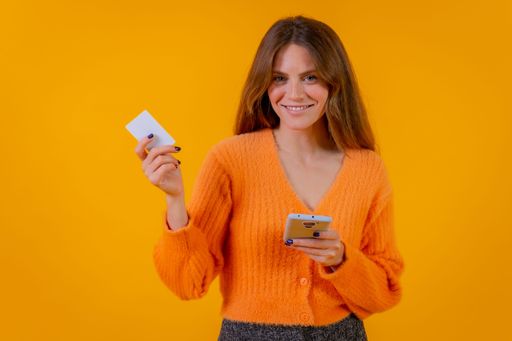 A young woman holding a smartphone on a yellow background - the concept of online shipping