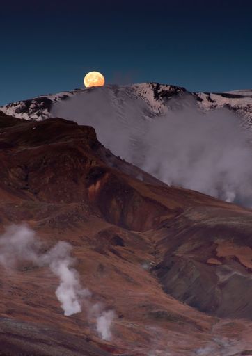 A vertical shot of mountains covered in smoke against a sky with a full moon.