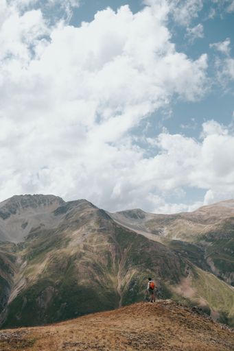 A vertical shot of a hiker standing on the edge of a peak with the view of the mountains.