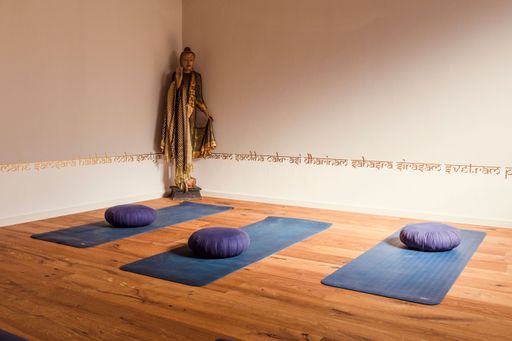A variety of yoga mats on a hardwood floor with the Buddha statue in the corner