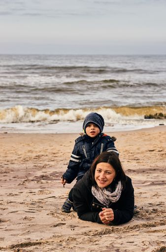 Woman and child laying on sand close by the water on a beach