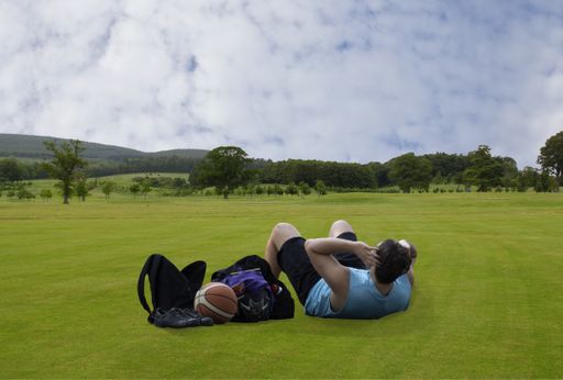 A shot of a single male doing gymnastics in the open air on a meadow under the cloudy sky