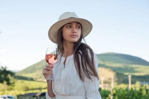 Portrait of beautiful brunette woman having wine outdoors in the vineyards.