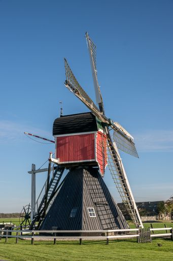 A vertical shot of post mill on a grassy field near wooden fences