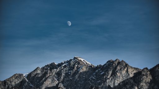 A scenic view of the moon rising above a majestic mountain range.