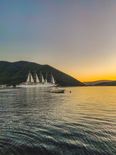 A vertical shot of a boat sailing on a calm sea over a background of mountains during a sunset