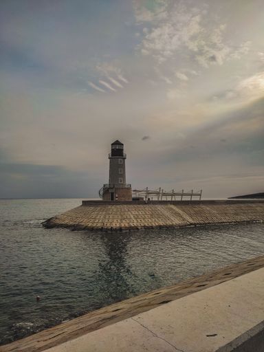 A vertical shot of a lighthouse near a sea over a background of a cloudy sky