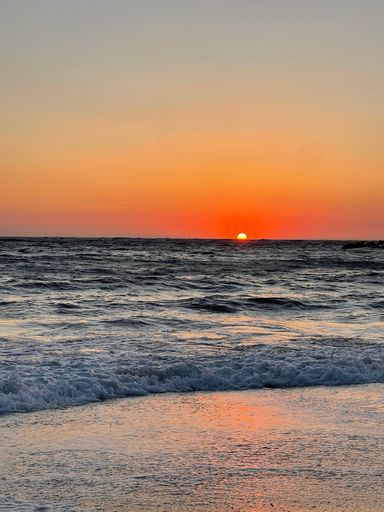 A vertical shot of a glowing bright orange sunset sky over a blue sea
