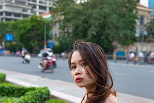 A shallow focus shot of an Asian female posing at the camera with motorcycles in the background