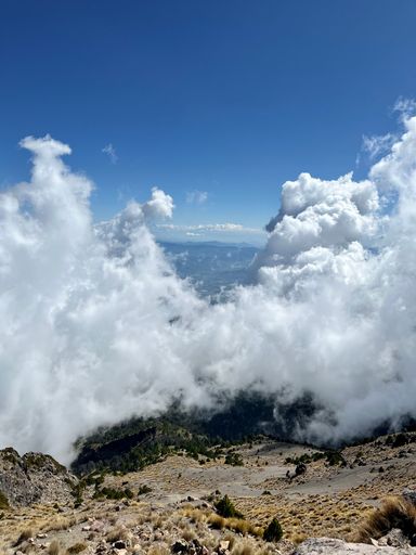 A vertical shot of the erupting Nevada de Colima volcano in Mexico with the blue sky in the background