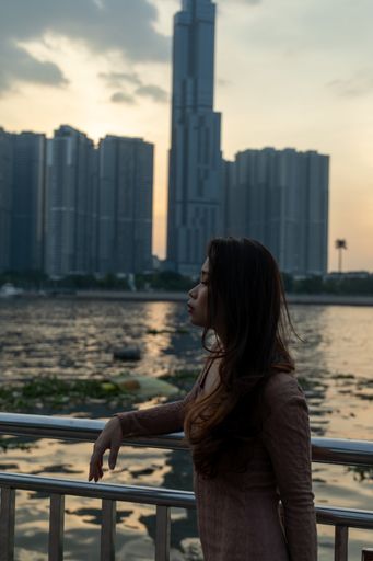 An attractive Asian female posing in front of a lake and skyscrapers in the background during sunset