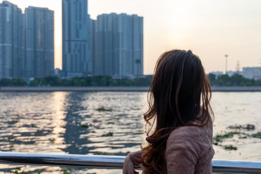 An attractive Asian female in a facial mask posing in front of a lake and skyscrapers during sunset - new normal concept