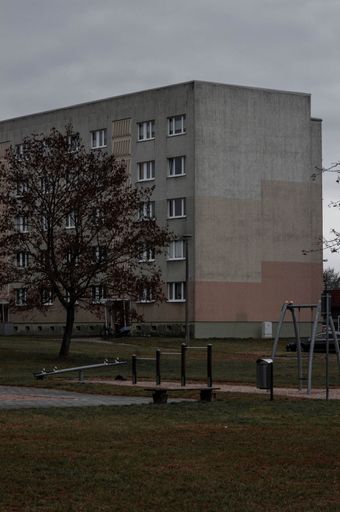 A view of an abandoned playground situated next to a dilapidated apartment complex with multiple windows, showing signs of neglect and disrepair