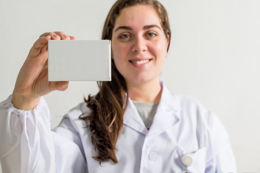 A smiling female doctor holding a pillbox while sitting in her consulting room