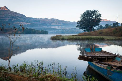 An idyllic landscape of Arthur Lake in Bhandardara, India, featuring a boat in the lake, rolling hills, and lush valleys