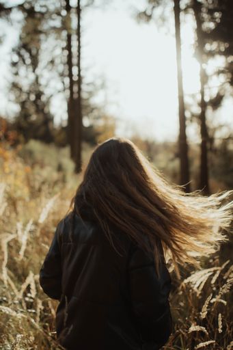 A vertical image of a woman with long, flowing hair walking through a lush, green forest on a sunny day