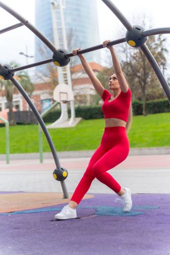 A vertical shot of a young woman in a red outfit doing arm exercises in a park. Healthy life concept.