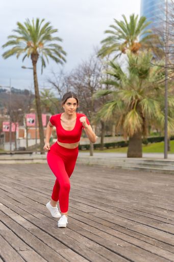 A young woman in a red outfit running in the city park. Fitness and healthy lifestyle concept.