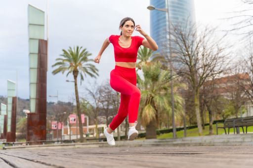 A young woman in a red outfit running in the city park. Fitness and healthy lifestyle concept.