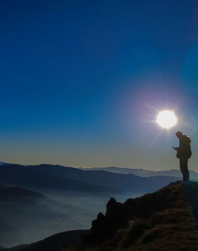 A Caucasian male stands on the edge of a rocky hill, camera in hand, and captures a stunning image of the landscape below