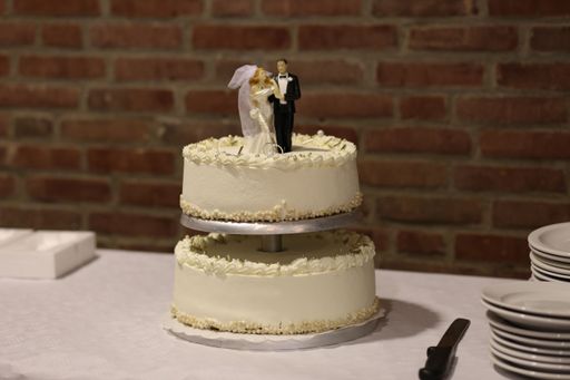 A two-tiered white wedding cake on a table, with a plate stacked nearby