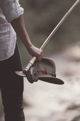A vertical shot of a male holding a fishing tackle and his hat against the isolated background