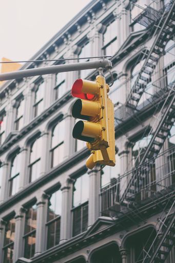A vertical shot of hanging traffic lights with the red light on and a building in the background