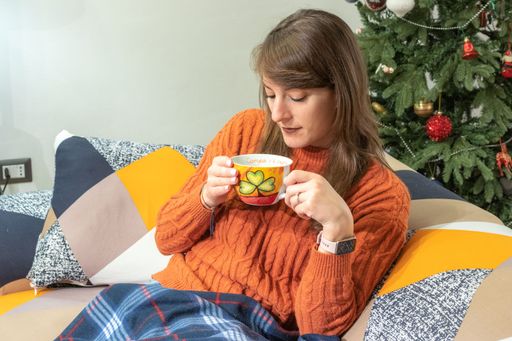 A closeup of an attractive Caucasian woman with a cup of tea in her hands against the Christmas tree