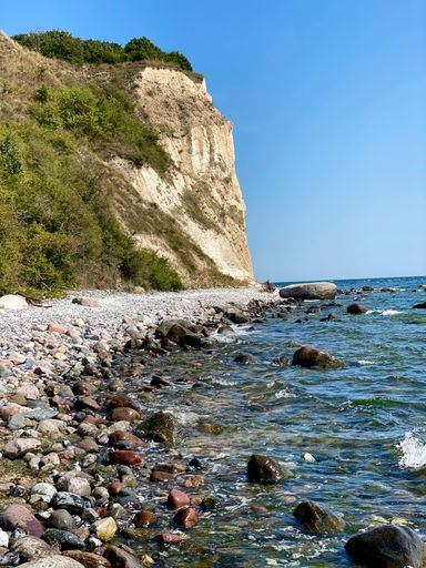 A scenic beachfront with a rocky shoreline, featuring large stones scattered across the sand