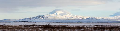 A panoramic shot of a mountain covered with snow under the blue sky and clouds