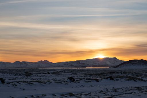 A scenic shot of a rocky mountains covered with snow under the golden sky at sunset