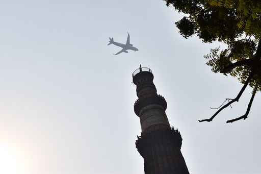 A low angle shot of an airplane flying over Qutub Minar